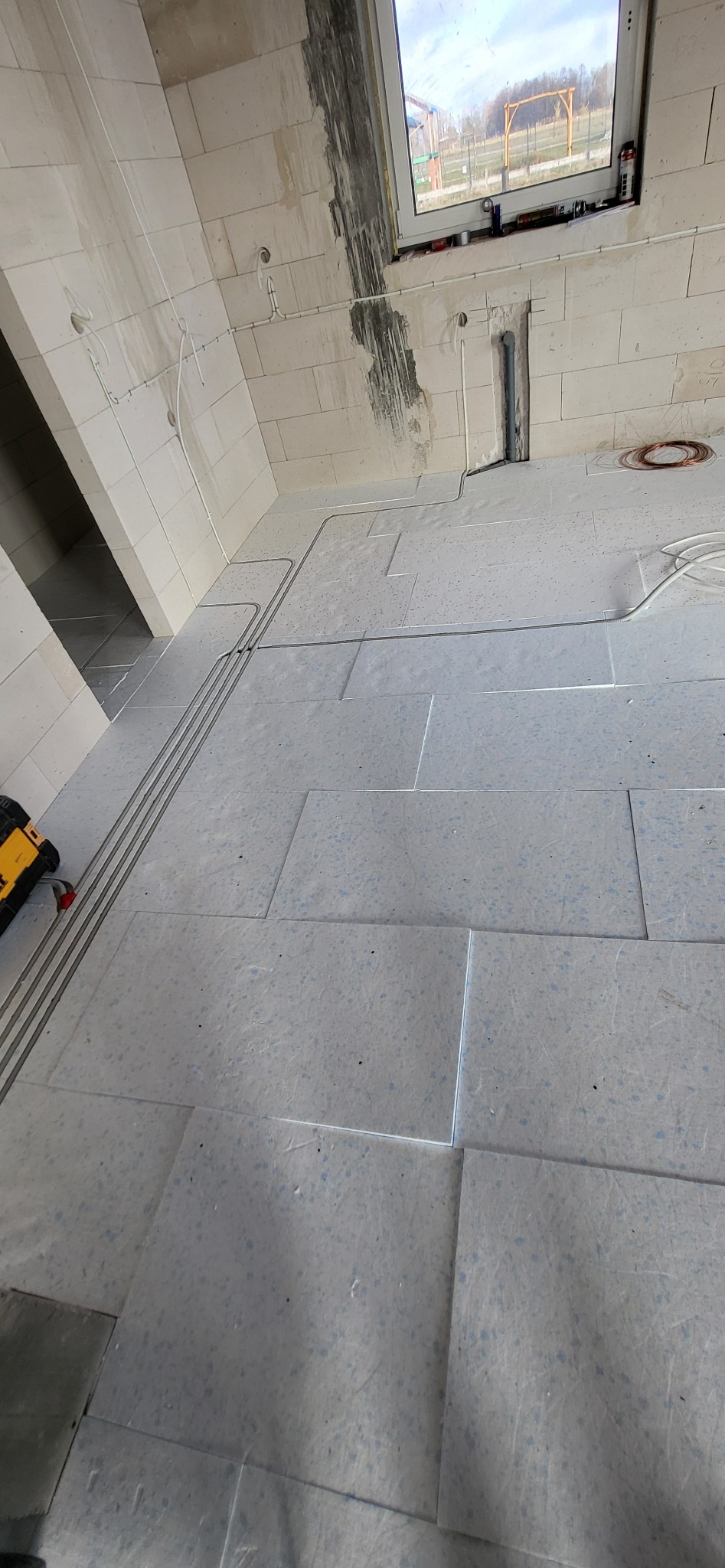 Wewnętrzne okablowanie elektryczne w rurkach ochronnych, ułożone na podłodze z płyt izolacyjnych w surowym stanie, widoczne przewody na ścianach i pod oknem.