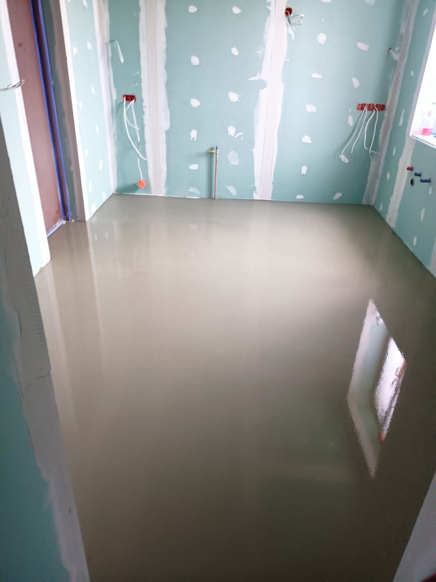 Wylewka samopoziomująca w łazience z przygotowanymi ścianami z płyt kartonowo-gipsowych, widoczne instalacje elektryczne i hydrauliczne.