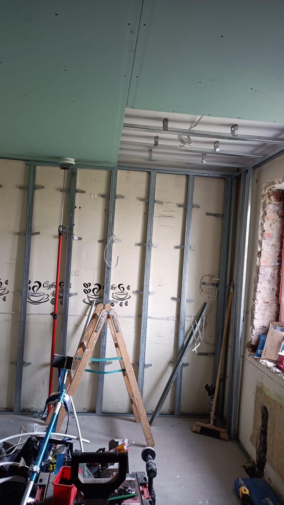 Wnętrze w trakcie montażu konstrukcji metalowej pod płyty gipsowo-kartonowe na ścianach i suficie, widoczne profile, instalacje, drabina i narzędzia na podłodze.