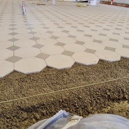Craftbud - Układanie podłogi z płytek w kształcie ośmiokątów i kwadratów na podsypce piaskowo-cementowej, widoczna linia poziomowania i akcesoria do układania płytek w tle.