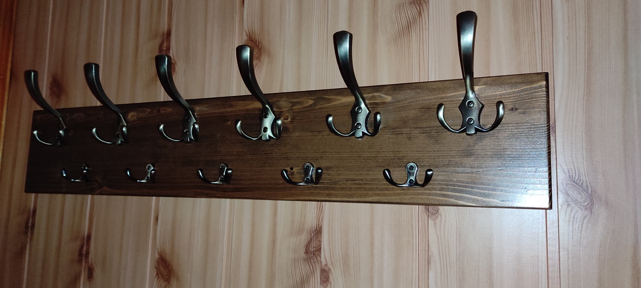 Drewniany wieszak na ubrania z metalowymi haczykami, zamontowany na ścianie z boazerii w odcieniach beżu i brązu.