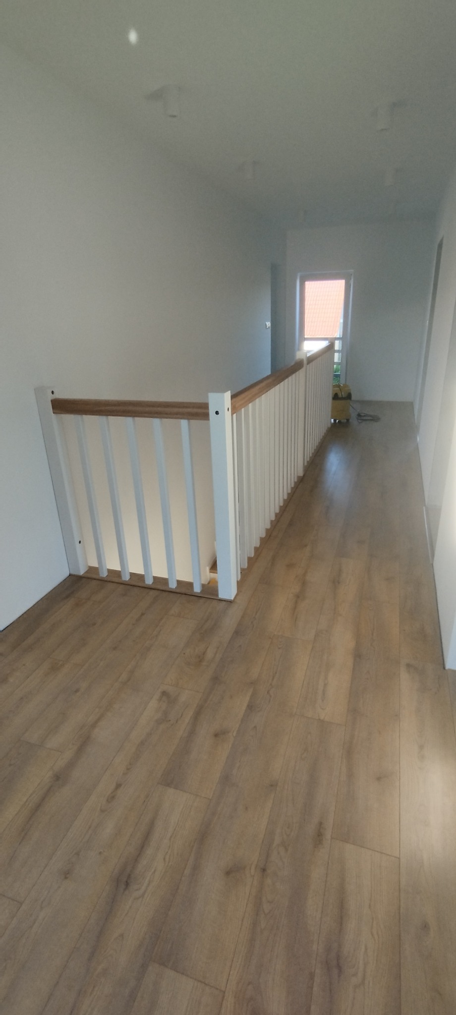 Korytarz na piętrze z drewnianą podłogą i białą balustradą z drewnianym poręczą, widok z góry na fragment korytarza.