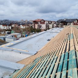 F.h.u. Adam Danczak - Konstrukcja więźby dachowej z desek impregnowanych na niebiesko, widok z góry na tle zabudowy Domaniewic i pochmurnego nieba.