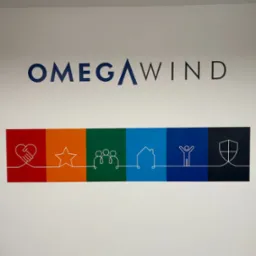 Ściana biura z namalowanym logo firmy Omega Wind, przedstawiającym kolorowe ikony: dłoń w dłoni, gwiazda, grupa os&oacute;b, dom, postać z podniesionymi rękami, tarcza.