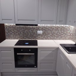 KUZ-BUD - Nowoczesna, szara kuchnia z okrągłą mozaiką na ścianie, czarnym zlewem i płytą indukcyjną, oświetleniem LED pod szafkami i drewnianą okładziną ścienną