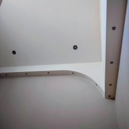 KUZ-BUD - Białe, nowoczesne wnętrze z podwieszanym sufitem i oświetleniem punktowym. Widok z dołu, podkreślający geometrię i minimalistyczny design.