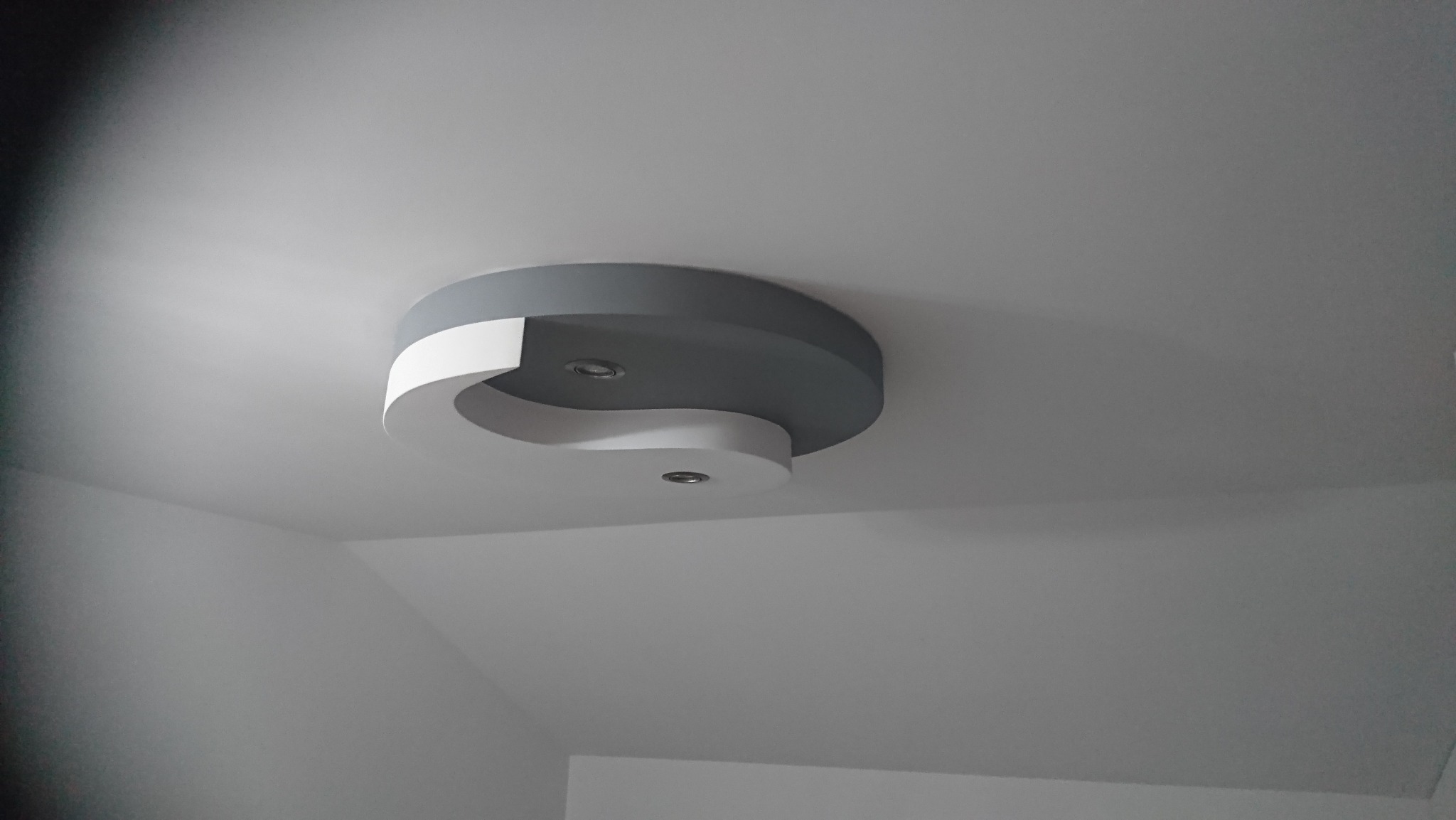 Okrągła, dwukolorowa (szara i biała) oprawa oświetleniowa sufitowa w kształcie symbolu Yin-Yang z dwoma punktami świetlnymi.