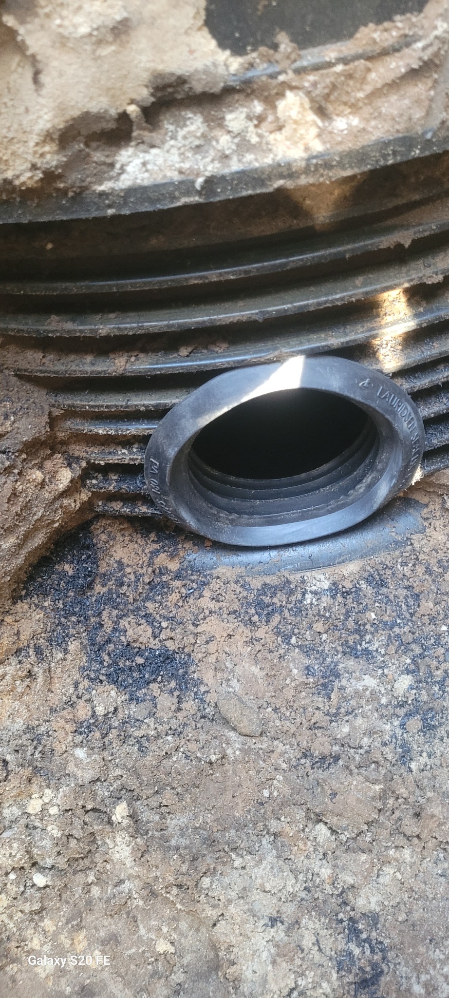 Fragment podziemnego przyłącza z czarnego karbowanego tworzywa sztucznego, wystający z ziemi, z widocznym otworem wlotowym.