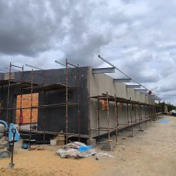 Wieczorek Budownictwo - Budowa domu w trakcie: ściany z bloczków, ocieplenie, rusztowania, widoczna betoniarka i narzędzia. Niebo pochmurne, teren budowy.