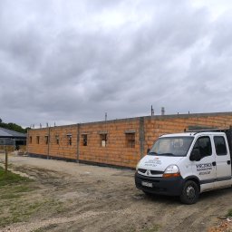 Wieczorek Budownictwo - Budowa budynku z cegły ceramicznej, widoczny mur z otworami okiennymi, na pierwszym planie samochód dostawczy z logo firmy budowlanej. Pochmurne niebo.