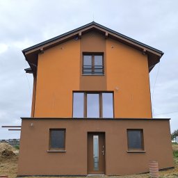 Wieczorek Budownictwo - Dwukondygnacyjny dom z elewacją w odcieniach brązu i pomarańczy, z widocznym stosem piasku obok, sugerujący prace budowlane w toku.