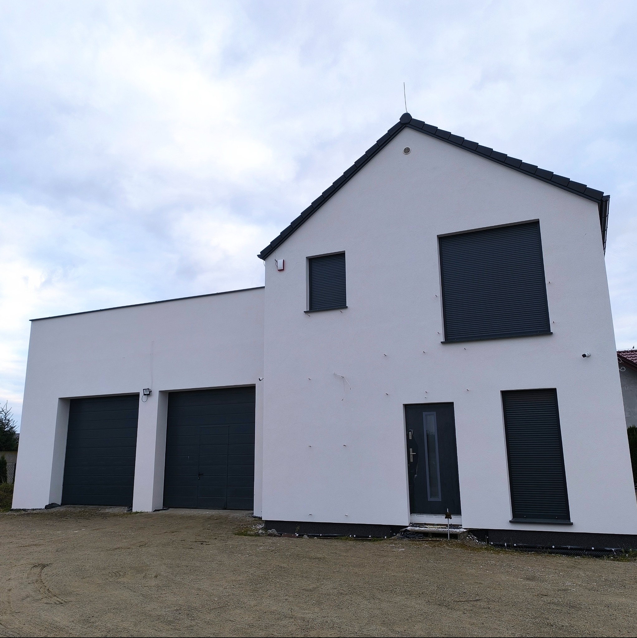 Nowoczesny dom z białymi ścianami, grafitową stolarką okienną i garażem dwustanowiskowym, widziany z zewnątrz. Minimalistyczny design i czysta elewacja.