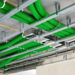 Zielone, karbowane rury wentylacyjne zamontowane pod sufitem w metalowej konstrukcji, widoczne żółte wypełnienia szczelin.