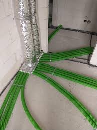 Rozprowadzenie zielonych rur wentylacyjnych z podłączeniem do srebrnego, elastycznego przewodu w surowym wnętrzu budynku.