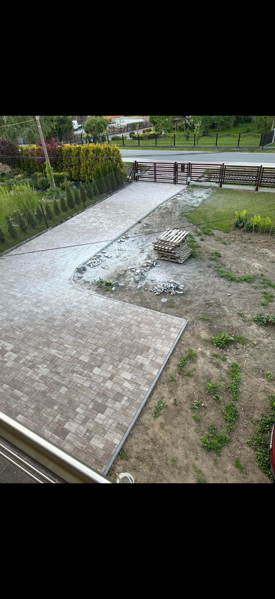 Układanie kostki brukowej w ogrodzie na posesji prywatnej, widok z góry na częściowo ułożoną nawierzchnię z paletami kostki i przygotowanym podłożem.