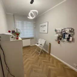 Ukończone układanie parkietu w jodełkę francuską i montaż listew przypodłogowych w pokoju z oknem i nowoczesną lampą. Widok na podłogę i część wyposażenia.