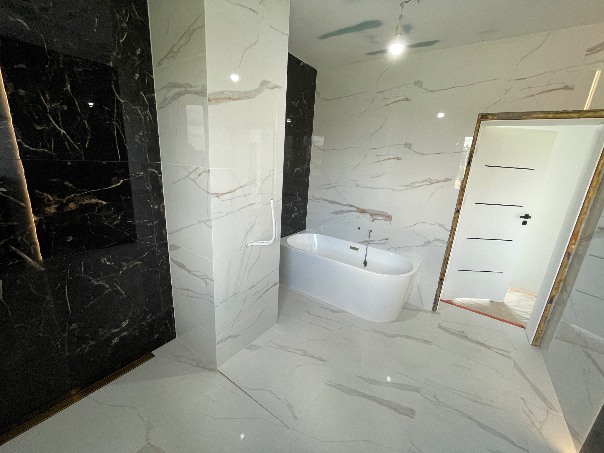 Luksusowa łazienka z białą wanną wolnostojącą i marmurowymi płytkami w odcieniach bieli i czerni. Widoczna minimalistyczna armatura i oświetlenie.