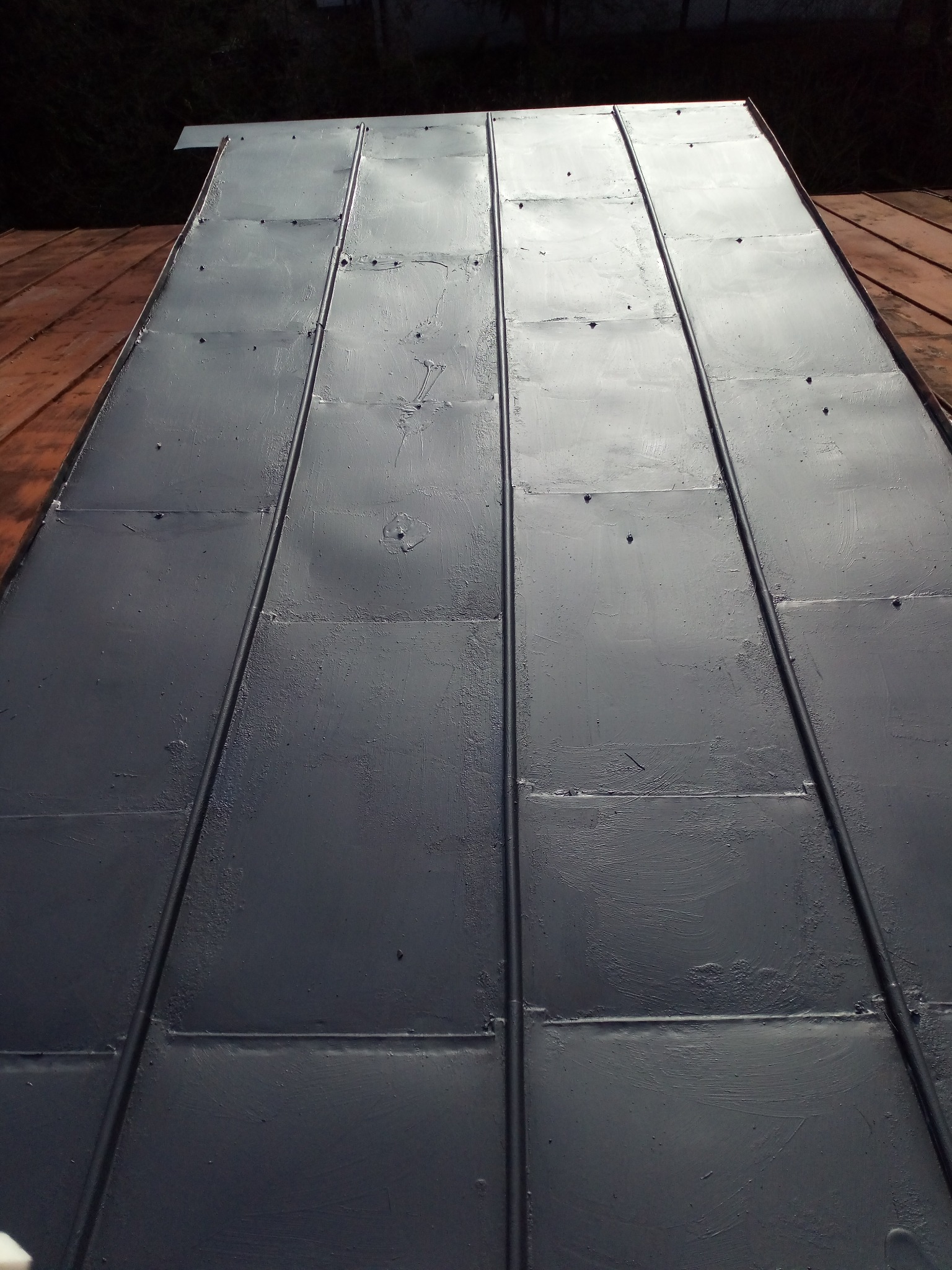 Szare, metalowe panele na dachu po świeżym pomalowaniu, widoczne ślady pędzla i łączenia paneli.