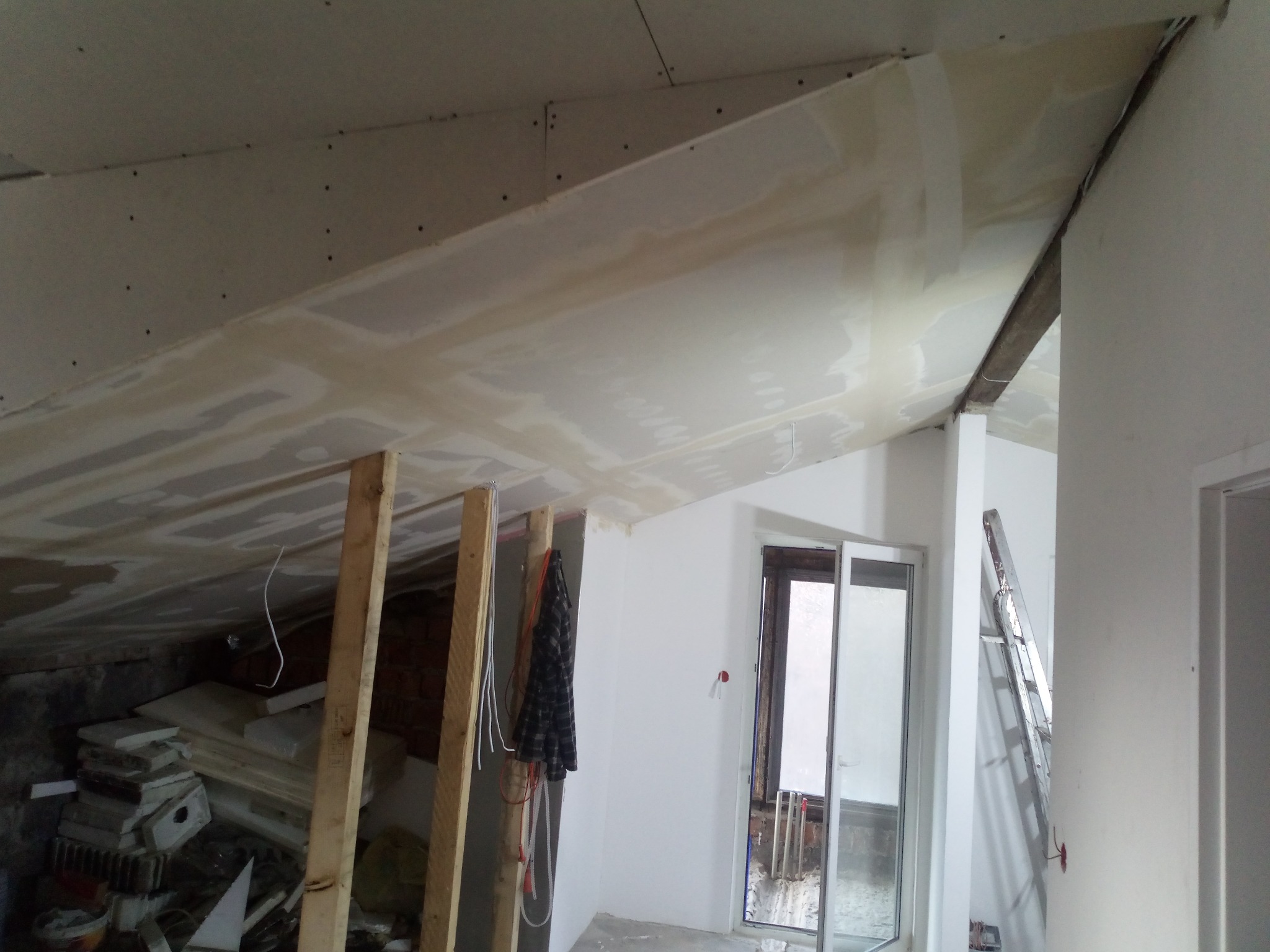 Skośny sufit poddasza w Łodzi w trakcie montażu płyt karton gips, widoczne drewniane elementy konstrukcyjne i przygotowane płyty. Częściowo nałożona masa szpachlowa.