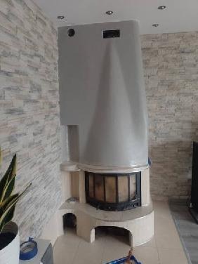 Otynkowany kominek w salonie z dekoracyjną ścianą z imitacji kamienia, widoczne akcesoria malarskie i zabezpieczenia podłoża.