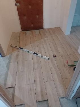 Układanie drewnianej podłogi w korytarzu, widoczna poziomica i miarka, surowy stan wykończenia ścian.