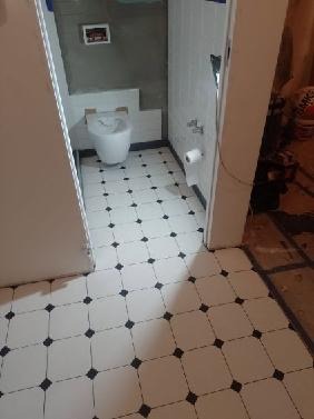 Wykończona łazienka z białą ceramiką i podłogą w biało-czarną szachownicę, widok z korytarza.