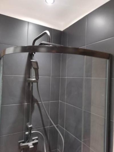 Szara łazienka z kabiną prysznicową z czarną ramą i baterią natryskową.