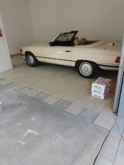 Układanie paneli podłogowych w garażu z widocznym samochodem kabrioletem, częściowo ułożone panele i paczki z panelami w rogu pomieszczenia.