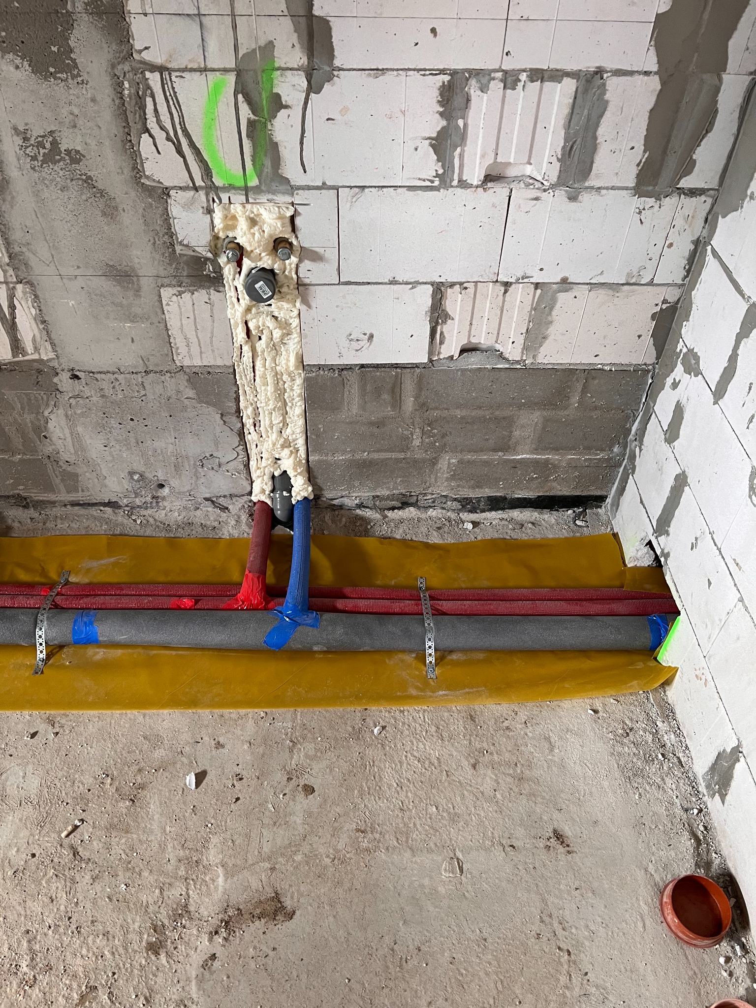Wewnętrzna instalacja wodna i grzewcza w trakcie montażu, rury zabezpieczone żółtą folią, pianka montażowa wokół rur przechodzących przez ścianę z betonu komórkowego.
