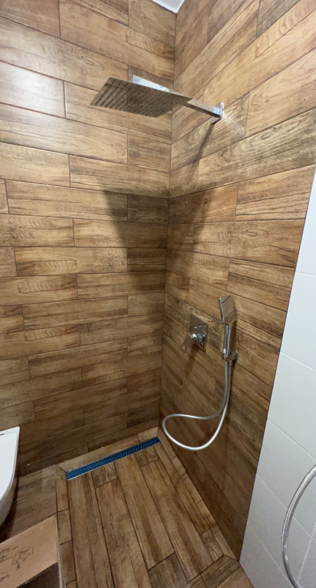 Nowoczesna kabina prysznicowa z deszczownicą i odpływem liniowym, wykończona płytkami imitującymi drewno.