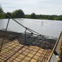 Wylewanie betonu na zbrojenie szkieletu budynku, widoczne narzędzia do rozprowadzania betonu i wystające pręty zbrojeniowe.