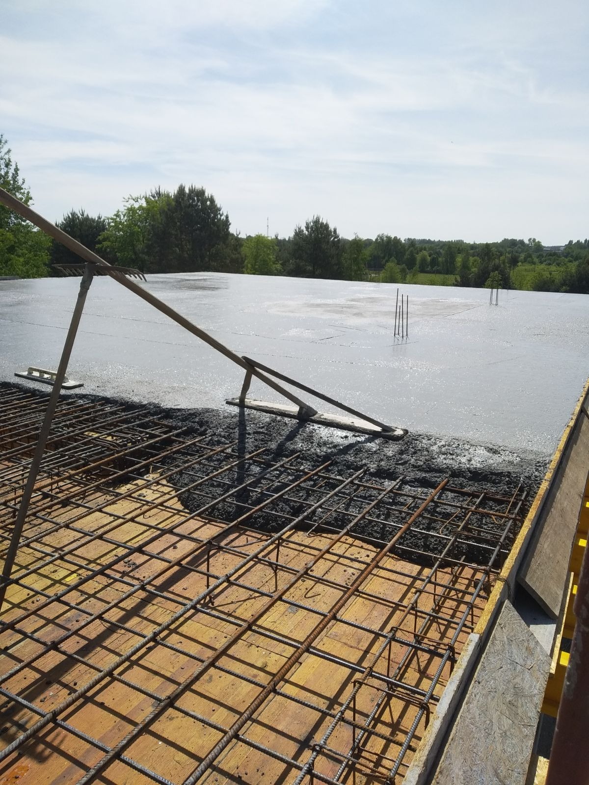 Wylewanie betonu na zbrojenie szkieletu budynku, widoczne narzędzia do rozprowadzania betonu i wystające pręty zbrojeniowe.