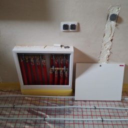 Drobne usługi hydrauliczne - Rozdzielacz ogrzewania podłogowego z czerwonymi rurami w szafce, widoczne rury ogrzewania podłogowego na folii. Usługa wykonana w Lublinie.
