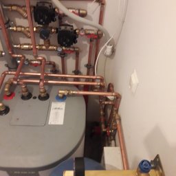 Drobne usługi hydrauliczne - Kompleksowa instalacja grzewcza z kotłem, rurami miedzianymi, zaworami i pompami obiegowymi w kotłowni. Widok z góry, oświetlenie sztuczne.