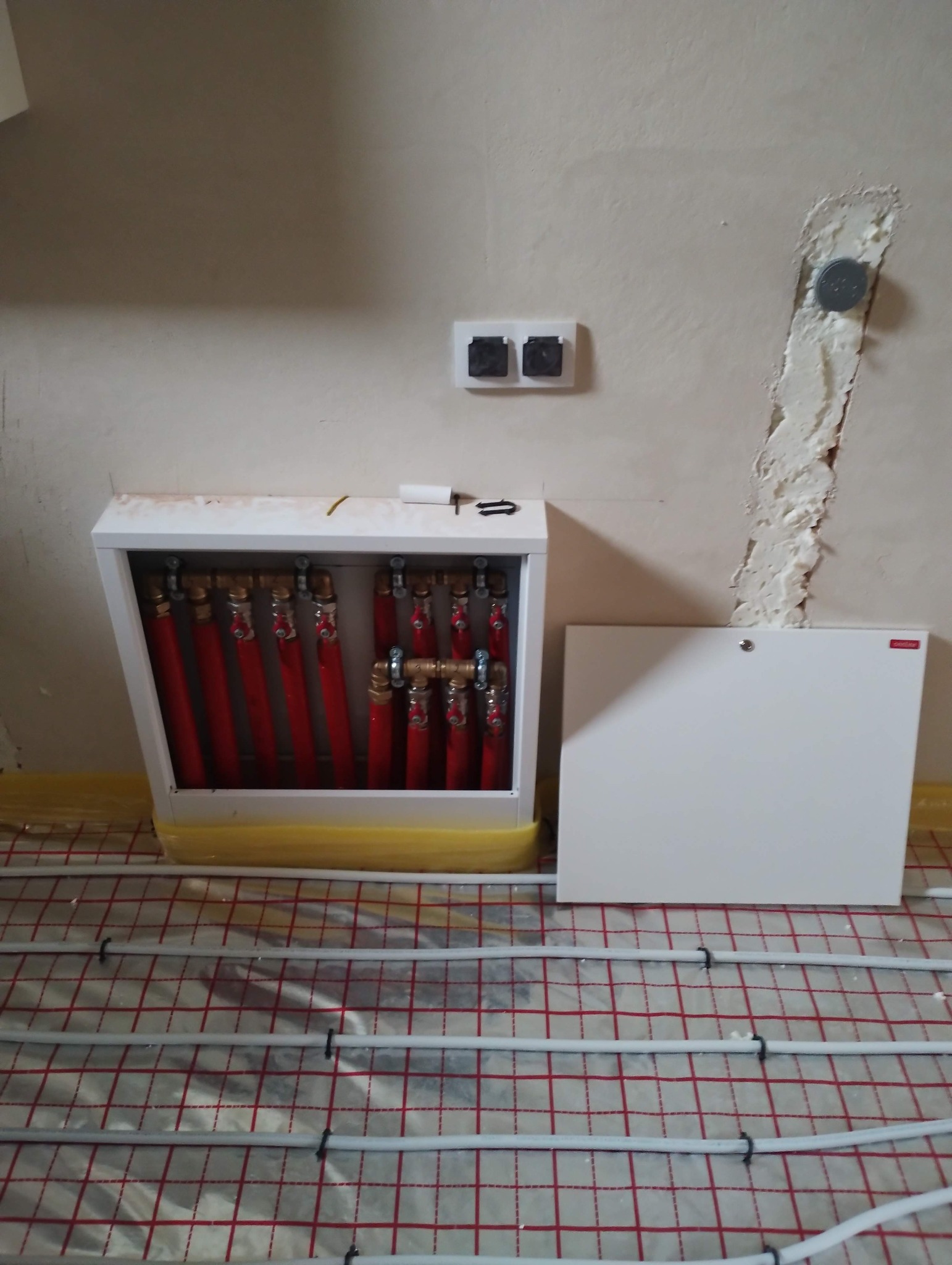 Rozdzielacz ogrzewania podłogowego z czerwonymi rurami w szafce, widoczne rury ogrzewania podłogowego na folii. Usługa wykonana w Lublinie.