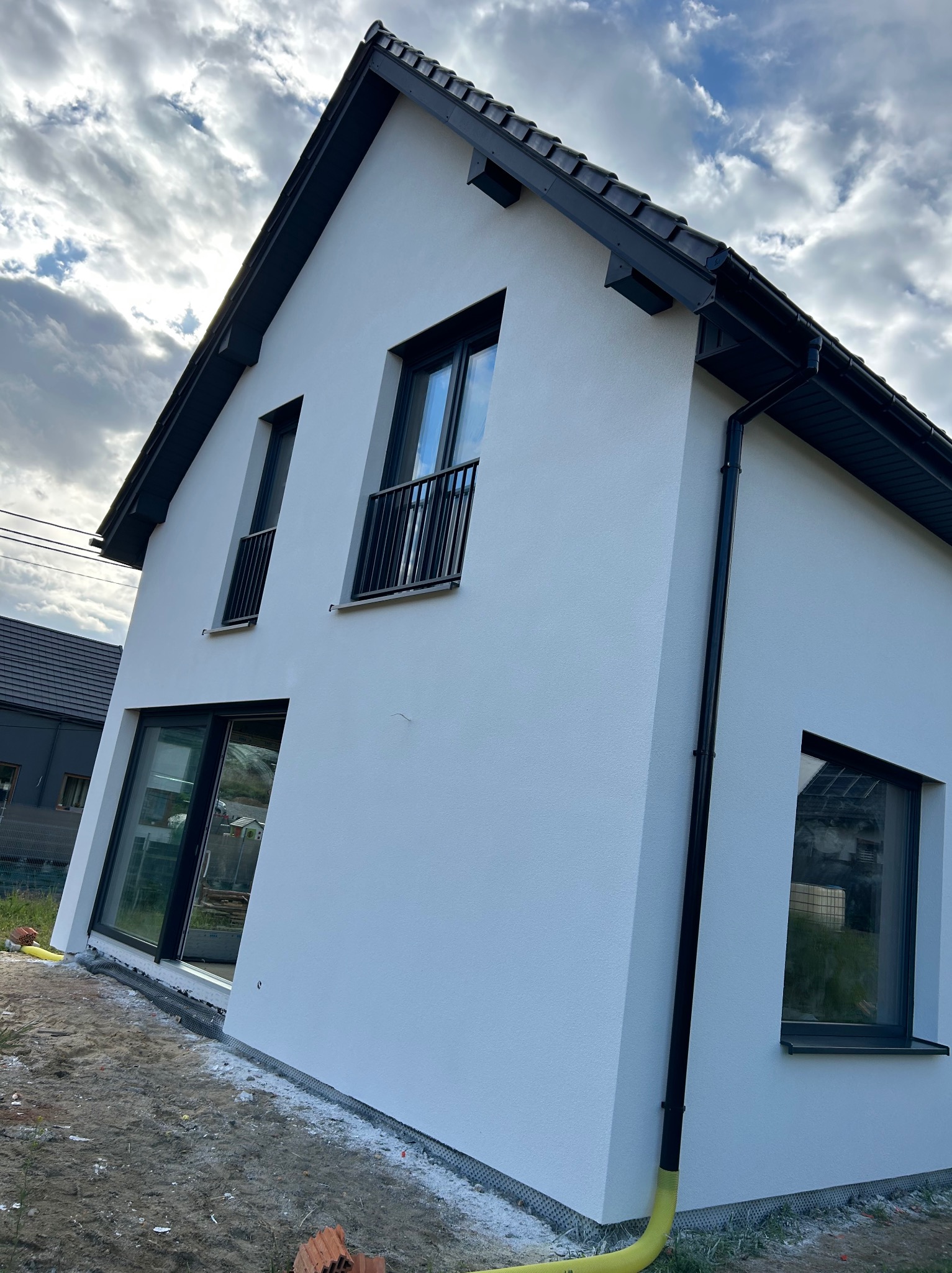 Nowoczesny dom z białą elewacją i czarnymi detalami, widok z zewnątrz. Kontrastowe kolory i minimalistyczny design podkreślają współczesny styl budynku.