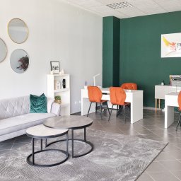 FENIKS Nieruchomości i Kredyty - Wnętrze biura nieruchomości z sofą, stolikami kawowymi i biurkami z krzesłami. Na ścianie logo firmy Feniks Nieruchomości i Kredyty. Nowoczesny design, stonowana kolorystyka.