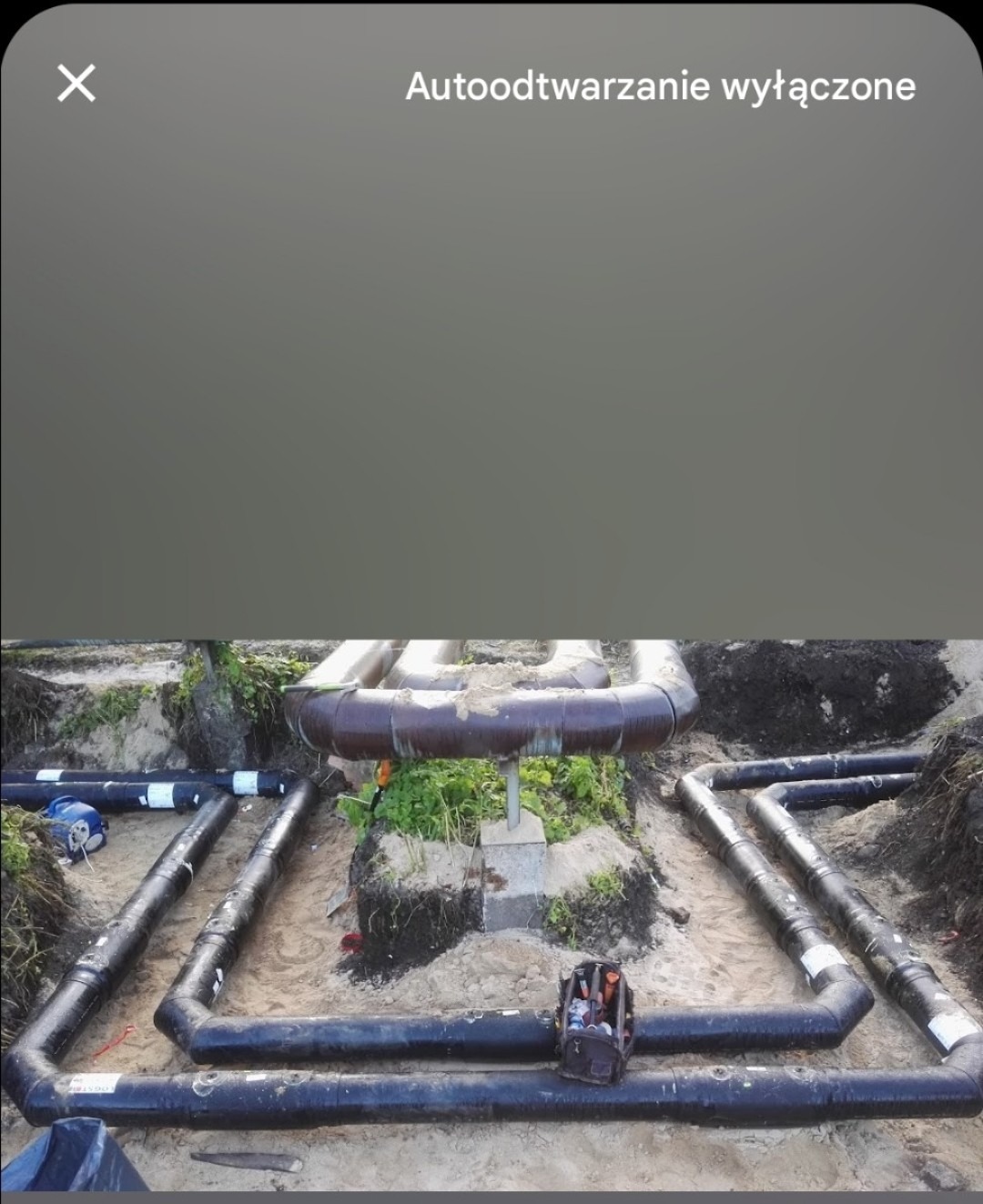 Instalacja rurociągu z czarnych rur w wykopie ziemnym, widoczne narzędzia w skrzynce obok rur.