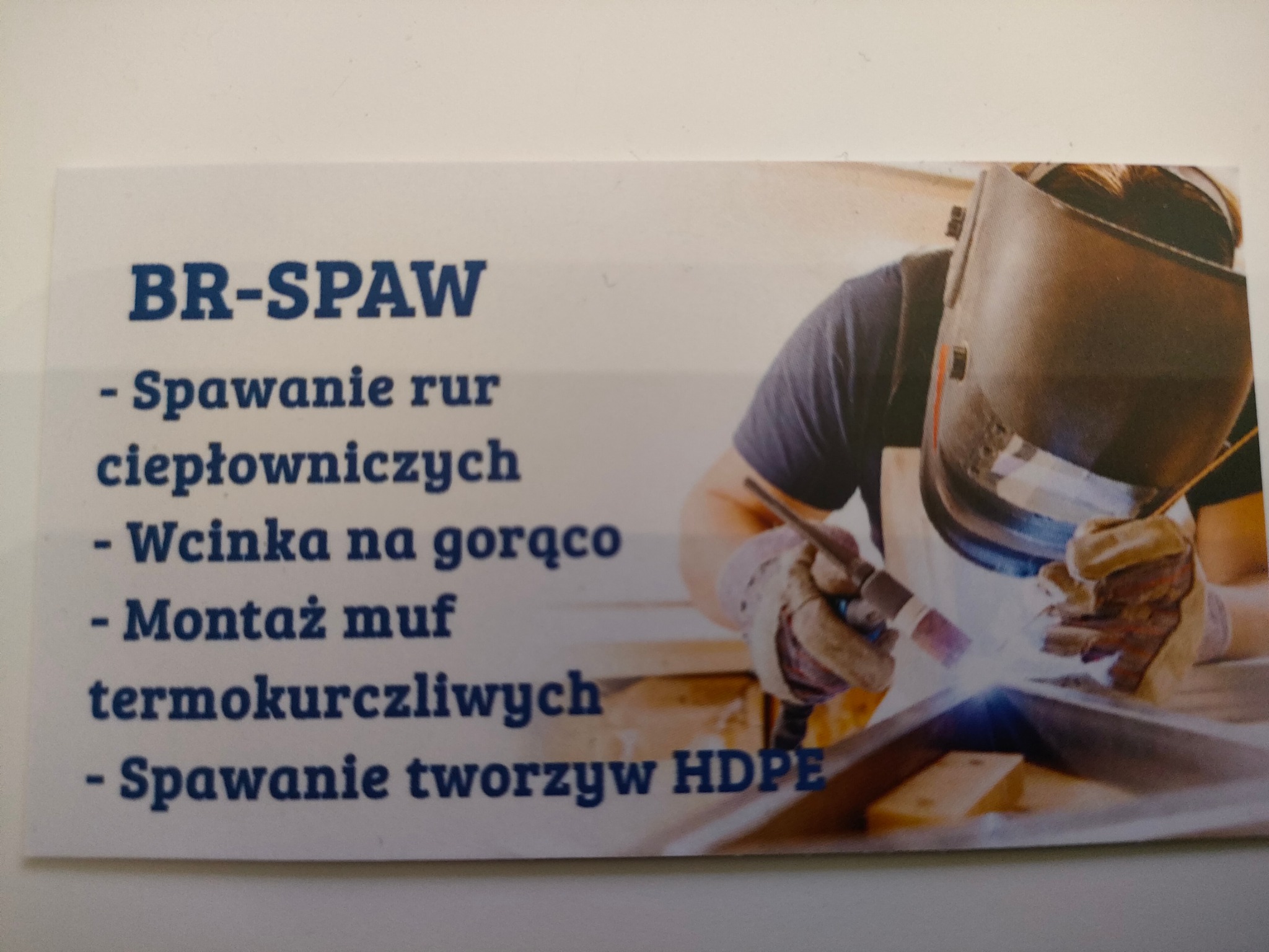 Wizytówka firmy BR-SPAW z ilustracją spawacza w masce podczas pracy, informująca o spawaniu rur ciepłowniczych, wcinaniu na gorąco, montażu muf termokurczliwych i spawaniu tworzyw HDPE.