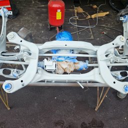 EMTE-SERWIS - Elementy zawieszenia samochodowego po piaskowaniu i malowaniu proszkowym, zabezpieczone folią, Wyględy. Widoczny również czerwony zbiornik piaskarki.