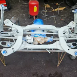 Elementy zawieszenia samochodowego po piaskowaniu i malowaniu proszkowym, zabezpieczone folią, Wyględy. Widoczny również czerwony zbiornik piaskarki.