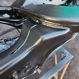 EMTE-SERWIS - Element podwozia samochodowego po zabezpieczeniu antykorozyjnym, z widocznymi śrubami i mocowaniami, ustawiony na metalowym stojaku.