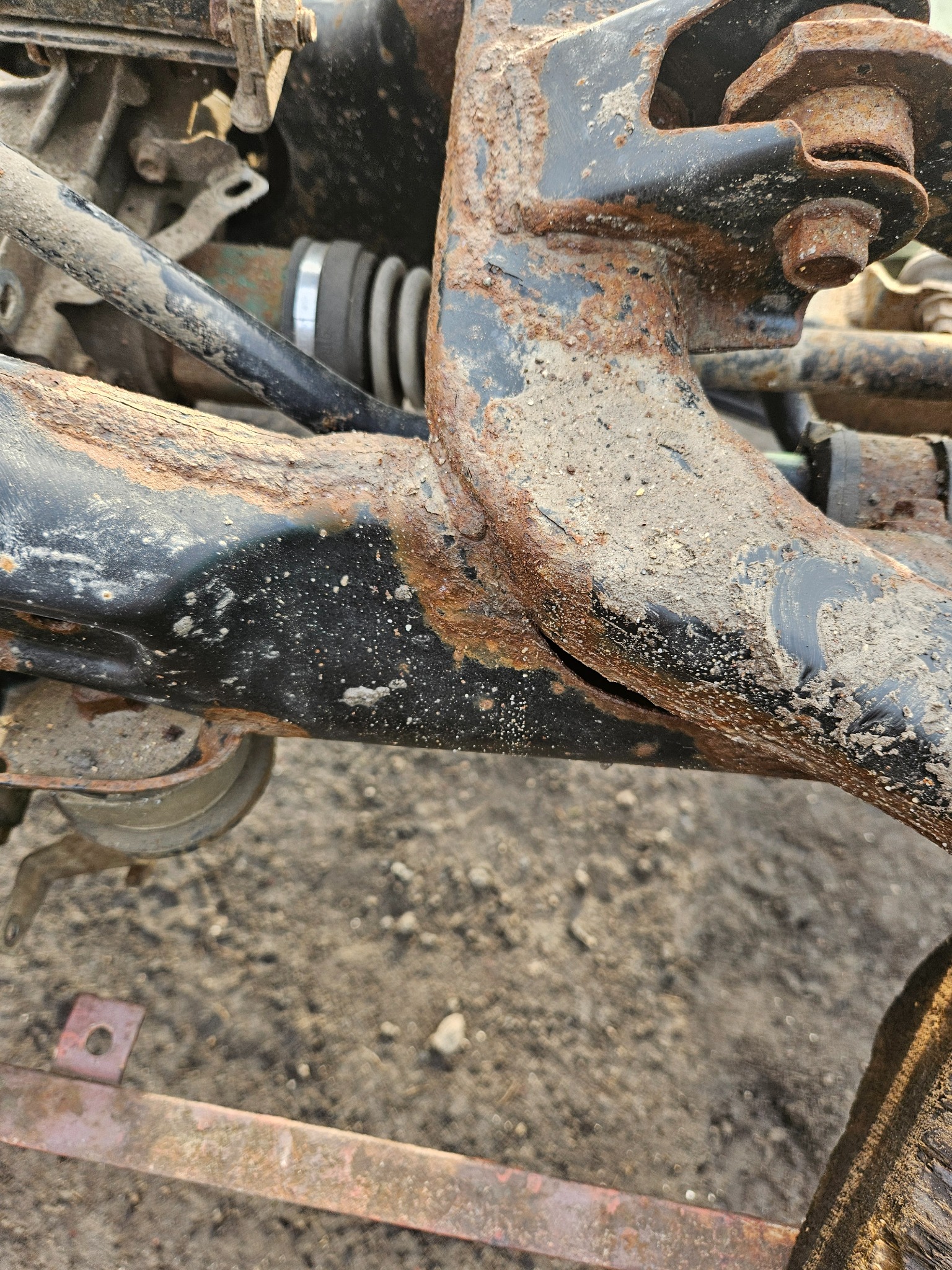 Zardzewiałe elementy podwozia samochodu, widoczne ślady korozji i zabrudzenia, w tle piasek.