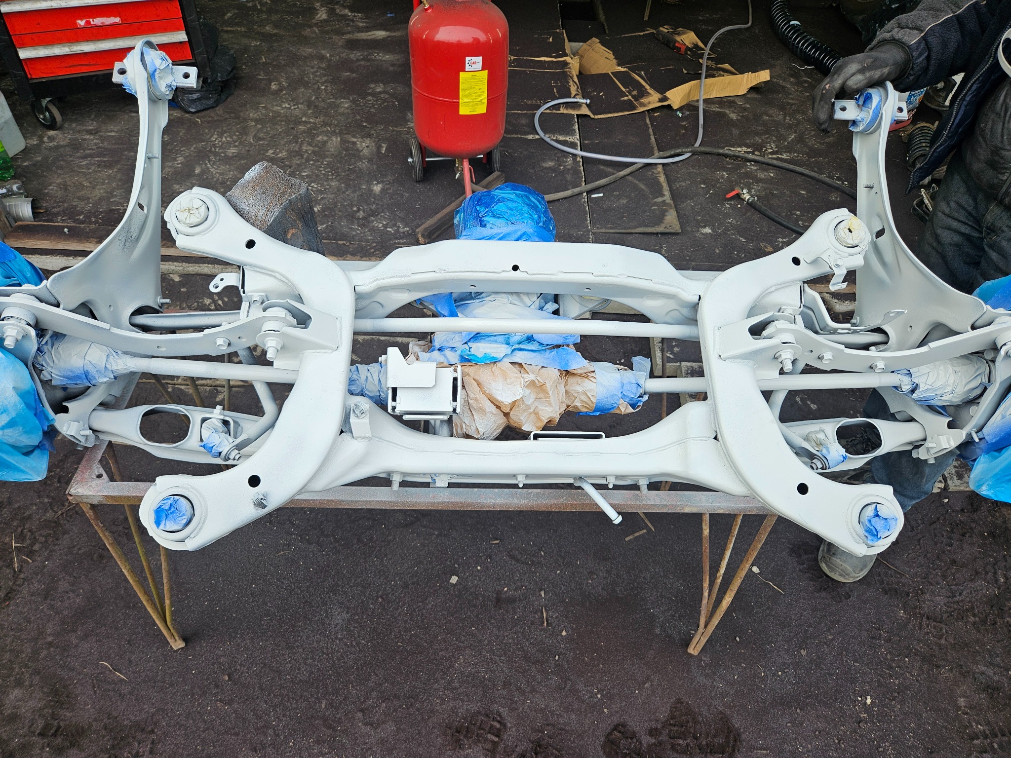 Elementy zawieszenia samochodowego po piaskowaniu i malowaniu proszkowym, zabezpieczone folią, Wyględy. Widoczny również czerwony zbiornik piaskarki.
