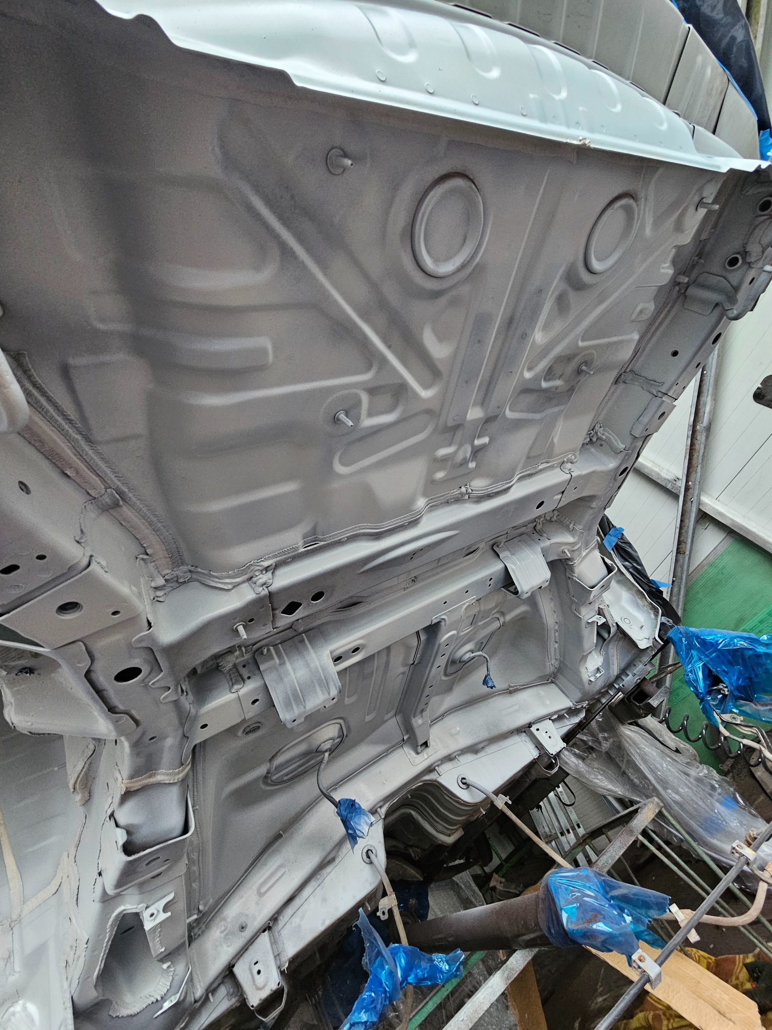 Podwozie samochodu po zabezpieczeniu antykorozyjnym, widoczne elementy konstrukcyjne pokryte srebrzystą powłoką ochronną, zabezpieczone elementy osprzętu w niebieskiej folii.