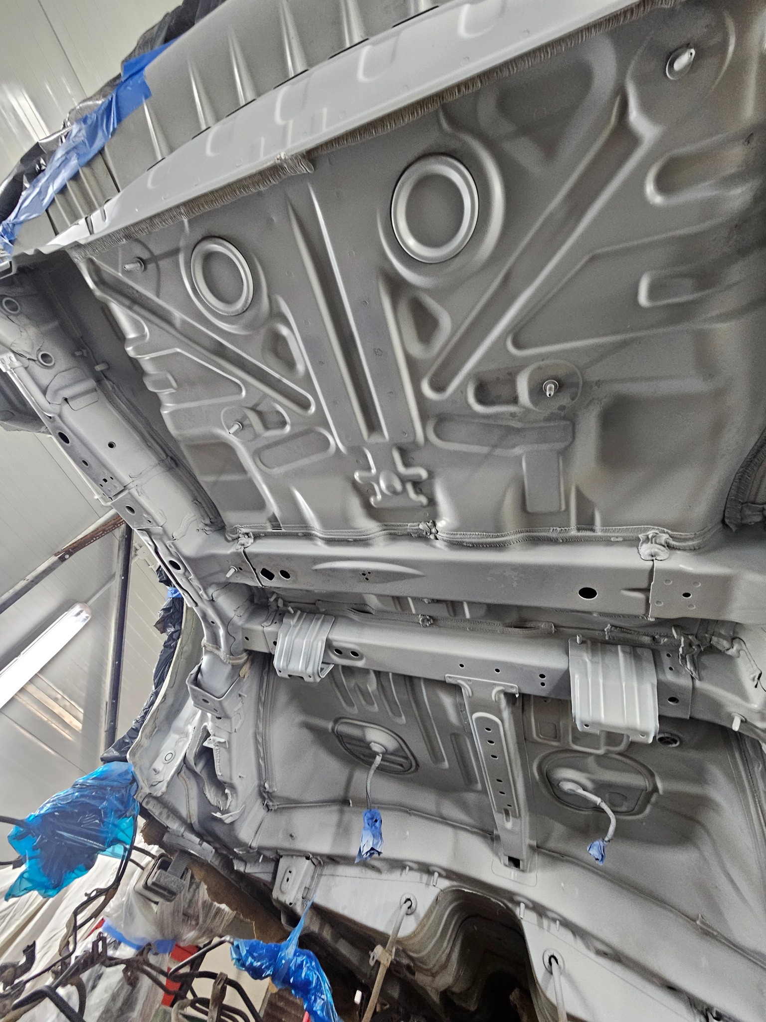 Spód samochodu po nałożeniu srebrnej powłoki ochronnej, widoczne zabezpieczenia folią i taśmą malarską na elementach.