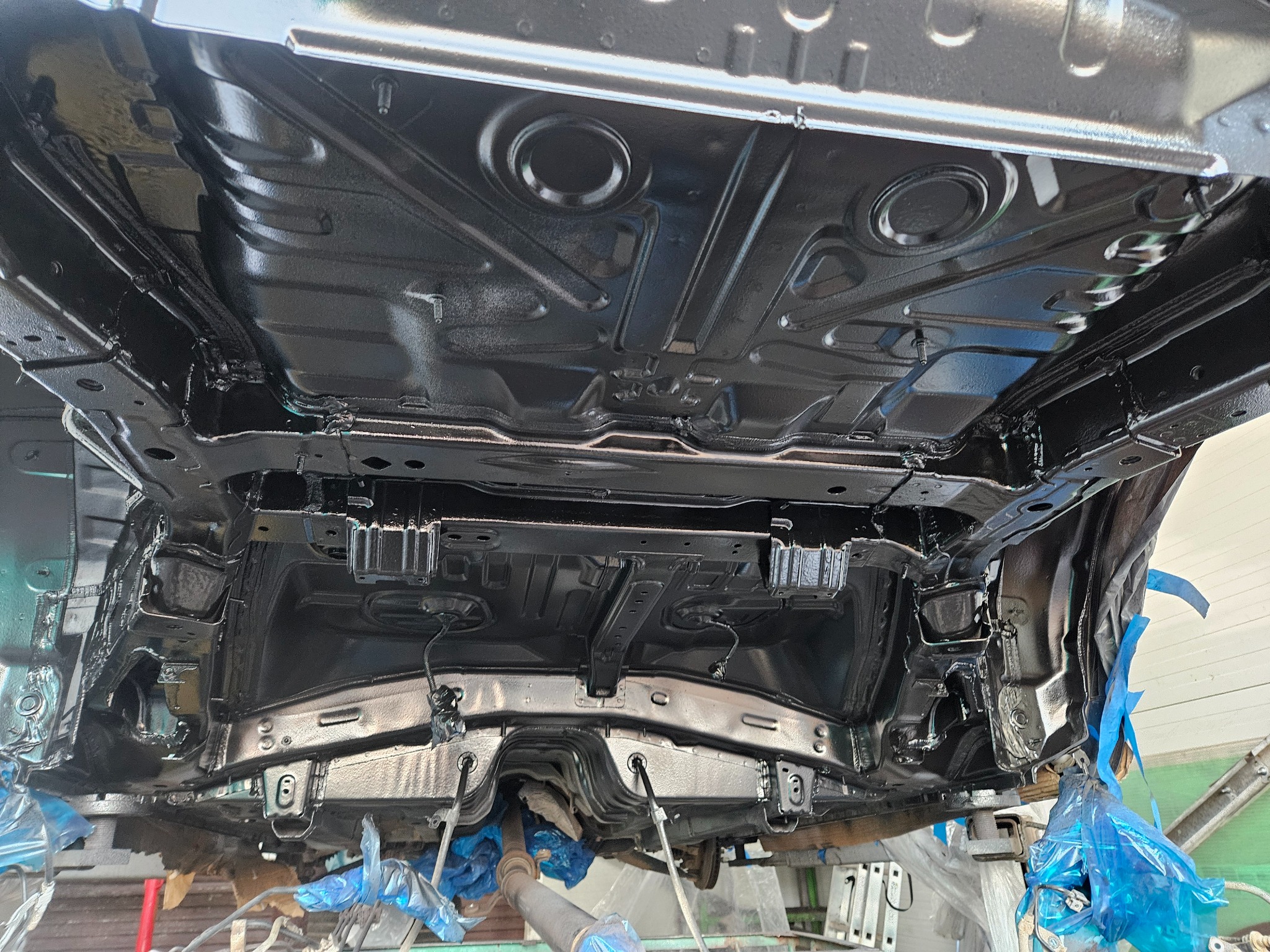 Podwozie samochodu po zabezpieczeniu antykorozyjnym, widoczne elementy zawieszenia i układu wydechowego, zabezpieczone folią elementy nadwozia.