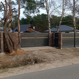 Usługi budowlane - Nowoczesne ogrodzenie panelowe z bramą przesuwną i furtką, z elementami imitującymi drewno, osadzone na betonowej podmurówce i słupkach z cegły klinkierowej, z drzewami wkomponowanymi w linię...