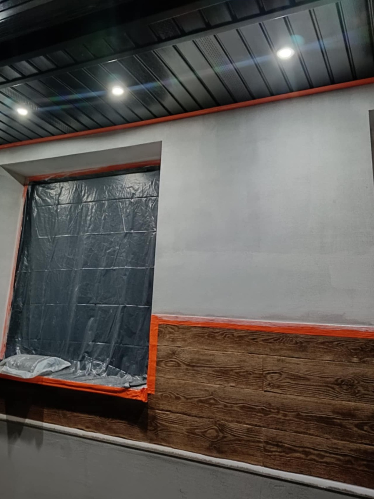 Przygotowania do prac elewacyjnych: okno zabezpieczone folią, fragment ściany z imitacją drewna, surowa ściana przygotowana do malowania.