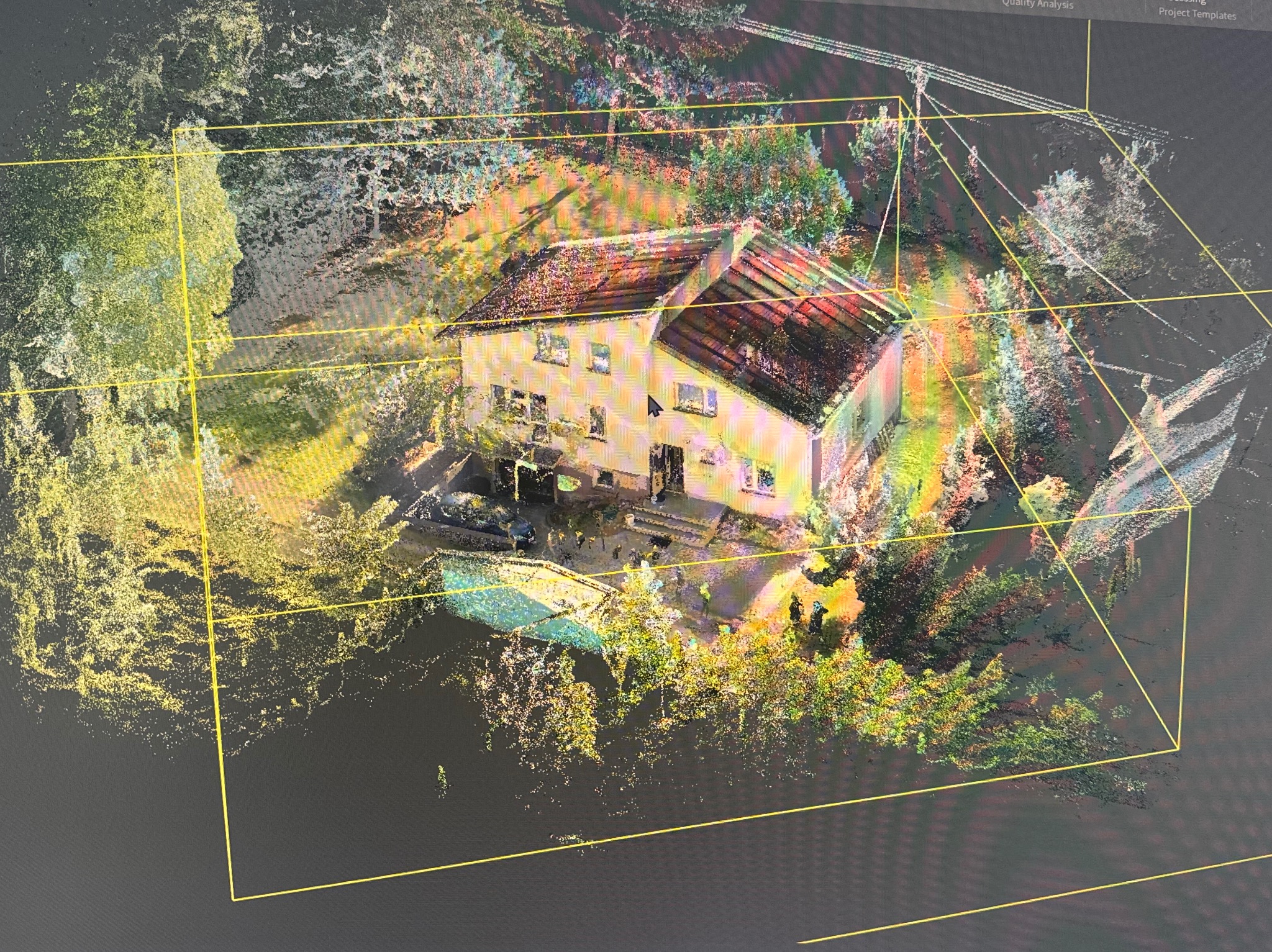 Skan 3D domu z otoczeniem, widok z góry, w żółtej ramce. Widoczny dach, elewacja, drzewa i krzewy. Na ekranie monitora widoczny kursor myszy.
